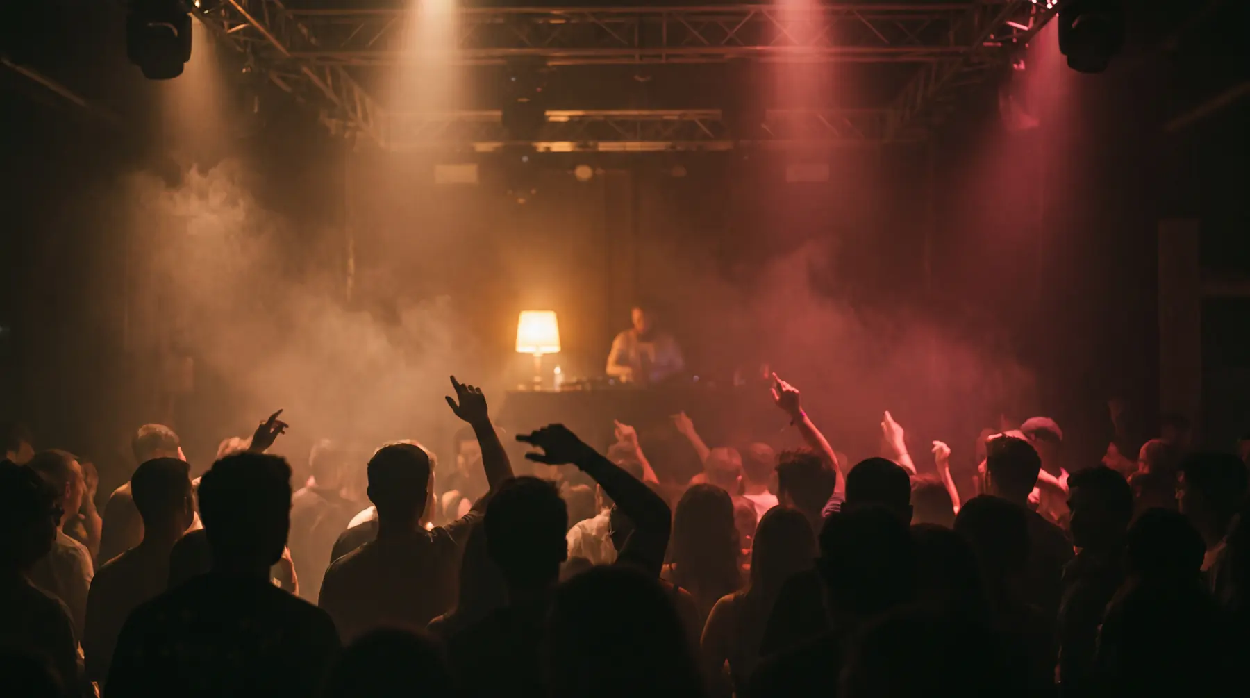 Volle donkere dansvloer met rook en warme lampen richting de dj-booth