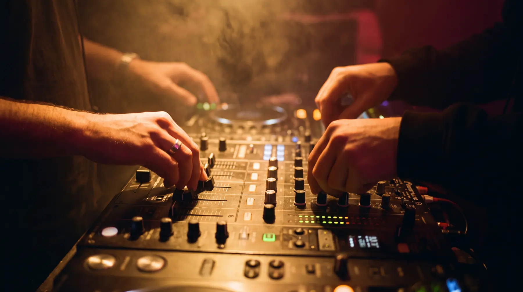 Vier handen tegelijk aan hetzelfde dj-mengpaneel in een donkere booth